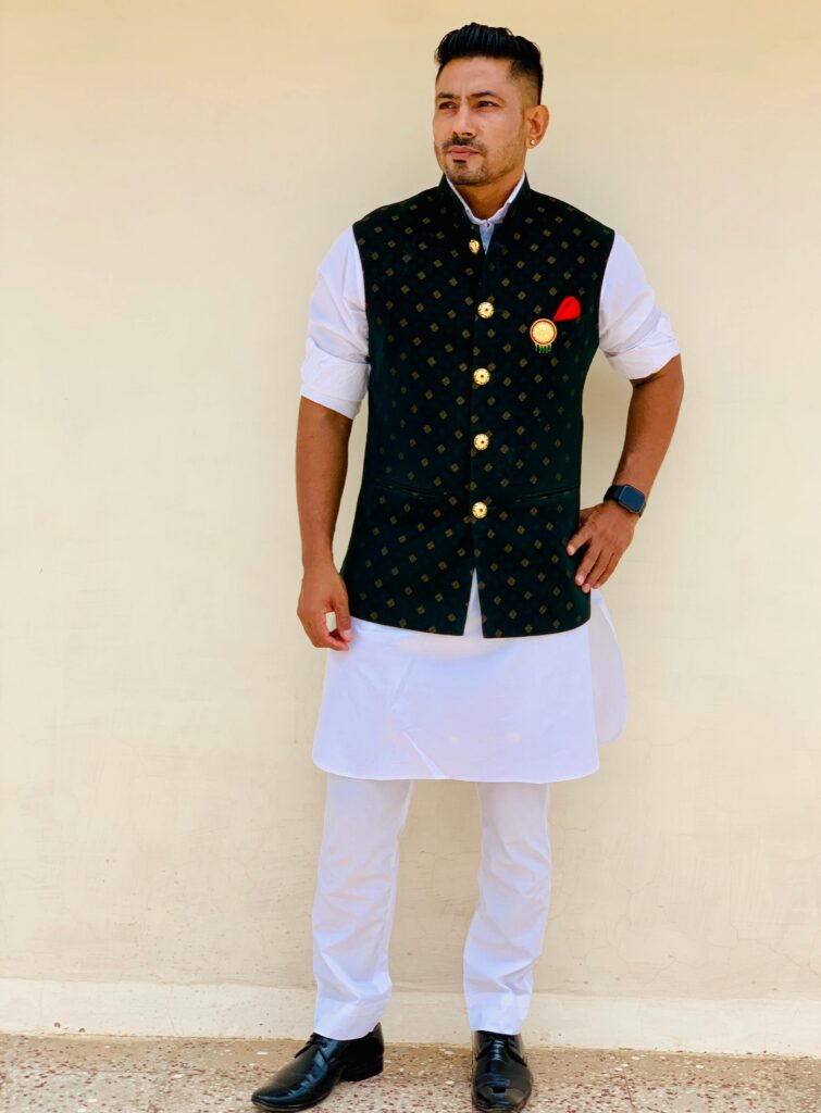 Indian groom in traditional attire posing against a wall in Jaipur.