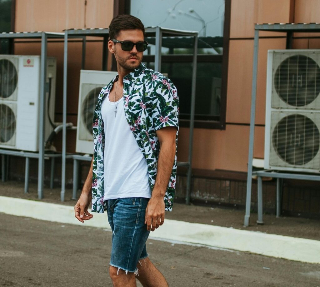 Fashionable man in sunglasses walking confidently along an urban street on a sunny day.