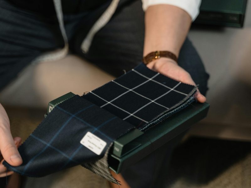 Tailor hands showcasing checkered fabric swatches for bespoke suit selection.